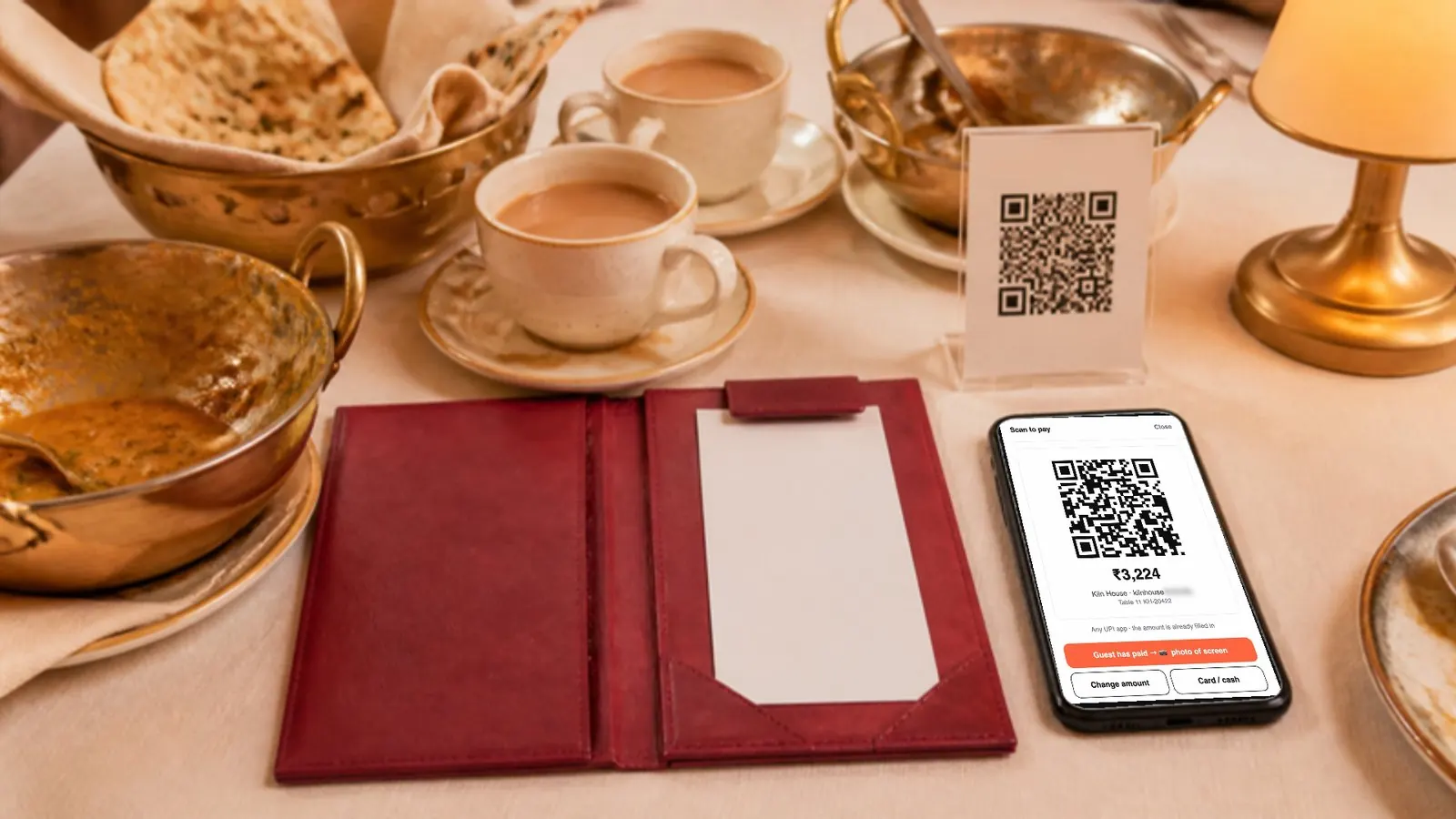 A restaurant table after dinner: an open bill folder, cups of chai, and a phone showing Nowish's Scan to pay screen for ₹3,224.